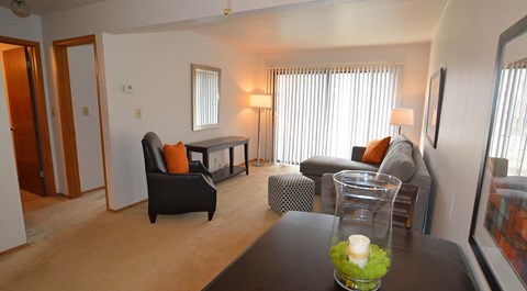 A living room with a black chair and a glass vase with a white candle on a table.