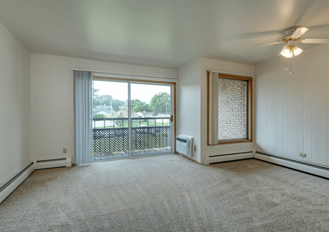 A room with a carpeted floor, a ceiling fan, and a sliding glass door leading to a balcony.