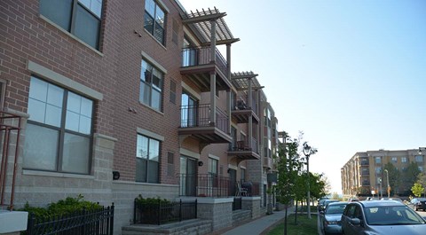 A row of apartment buildings with cars parked in front.