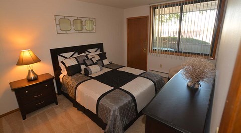 A bedroom with a bed, nightstand, and window.
