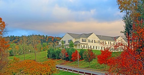 A large house with a grey roof is surrounded by trees with orange and red leaves.