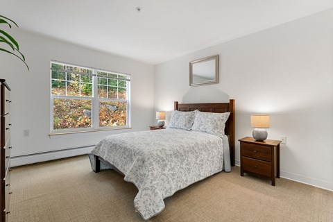 A bedroom with a bed, nightstand, and window.