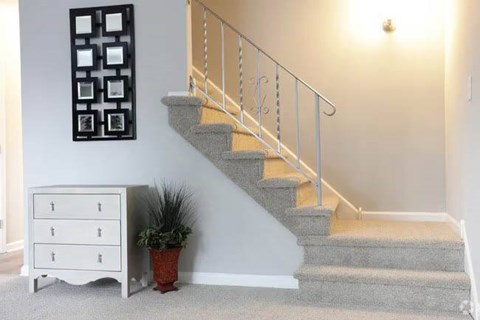 A staircase with a metal railing and a potted plant next to a white chest of drawers.