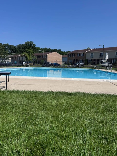 A swimming pool surrounded by a grassy area and buildings in the background.