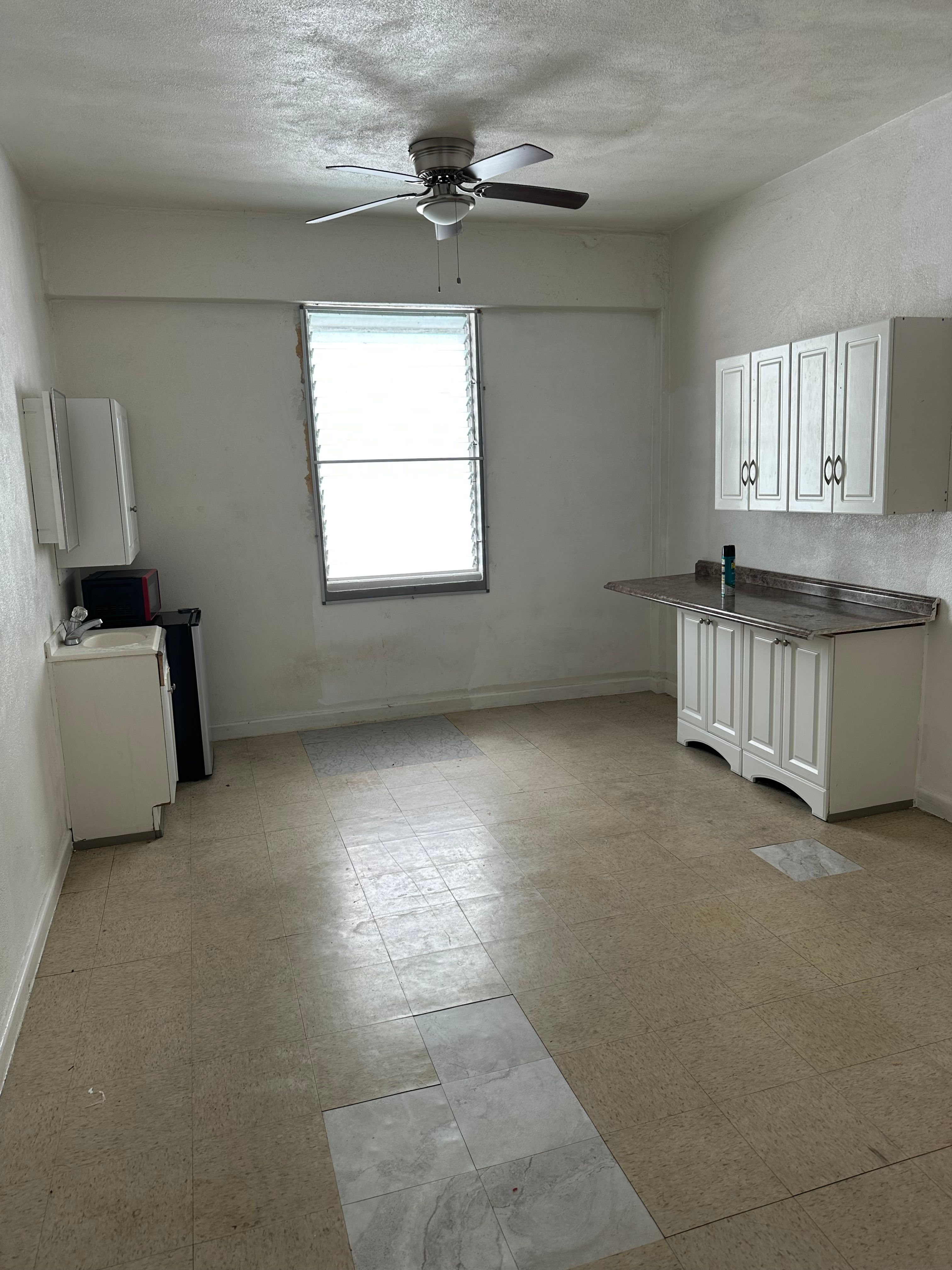 A room with a fan, a window, and a cabinet.