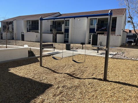 A playground with a swing set in front of a building.