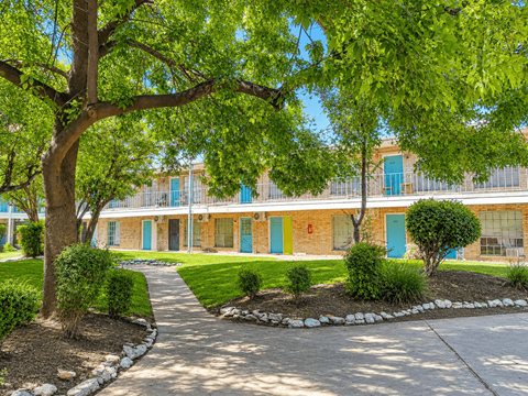 A tree with green leaves is in front of a building with blue doors.