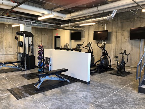 A gym with a variety of equipment including a bench, weights, and a television.