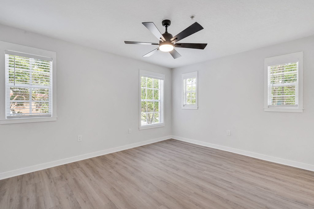 an empty bedroom with a ceiling fan and three windows