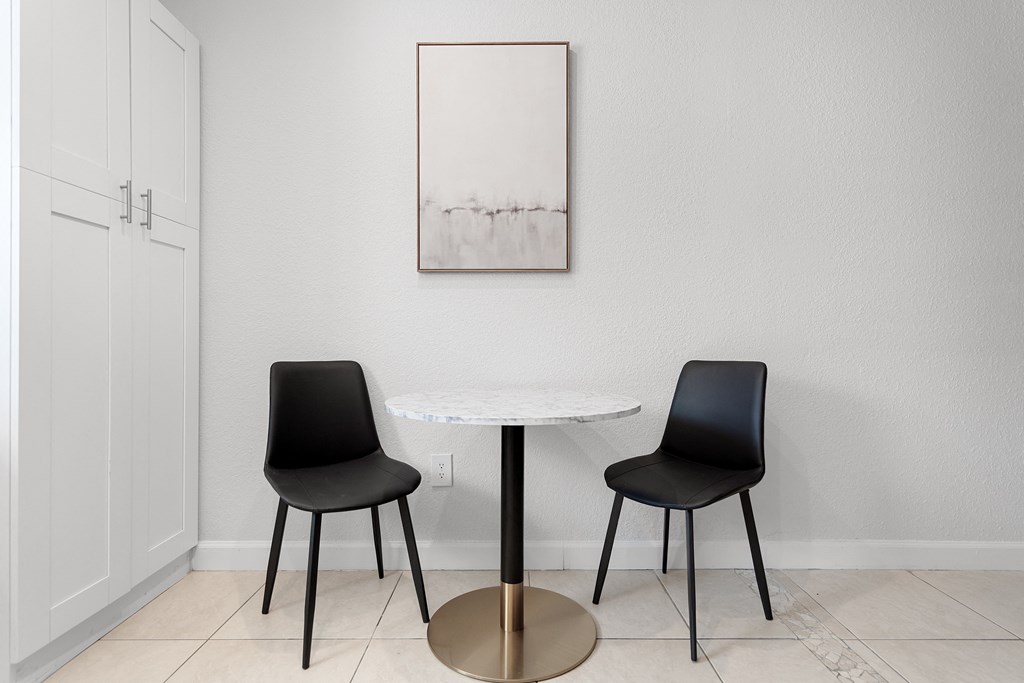 a small table with two black chairs and a painting on the wall