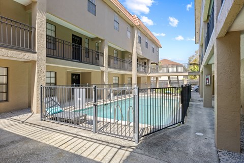 A pool surrounded by a black fence in a sunny courtyard.