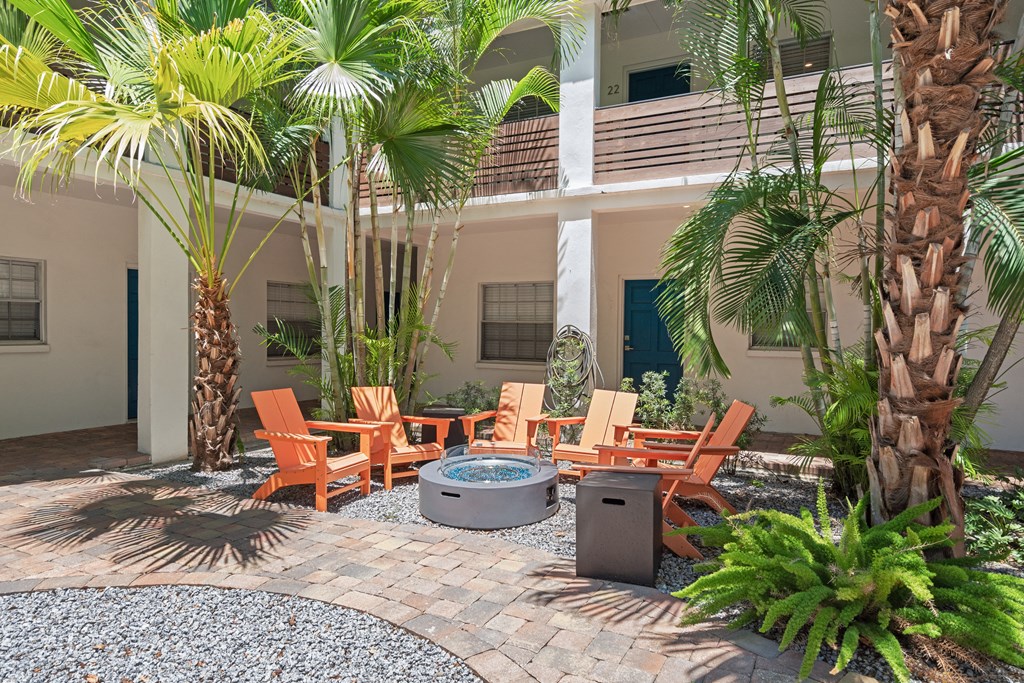 a patio with a fire pit and chairs in front of a building