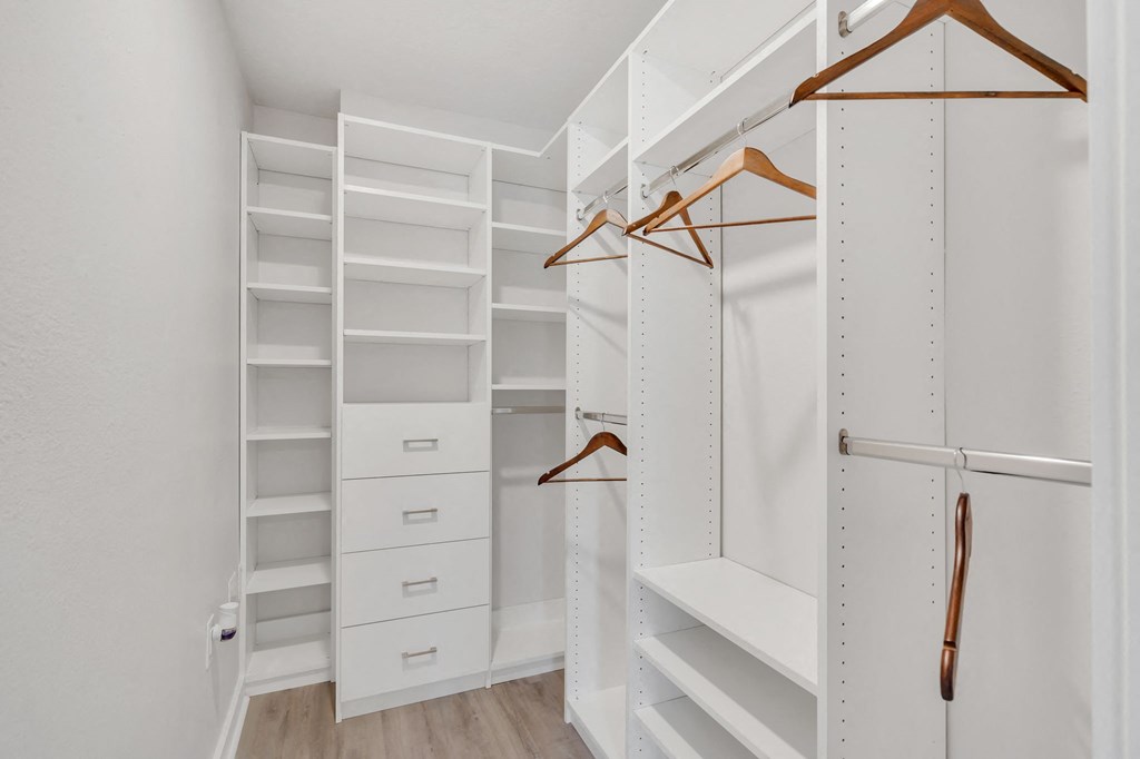 a walk in closet with white walls and wooden shelves and hangers