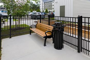 A black metal fence surrounds a wooden bench with a black trash can.