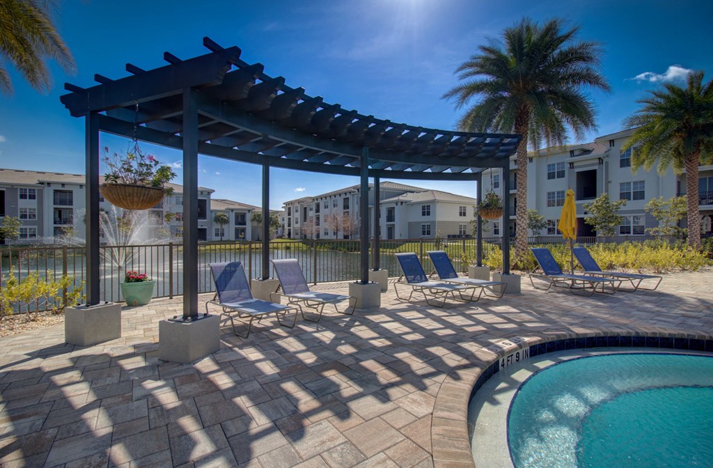 a patio with a pool and chairs under a pergola