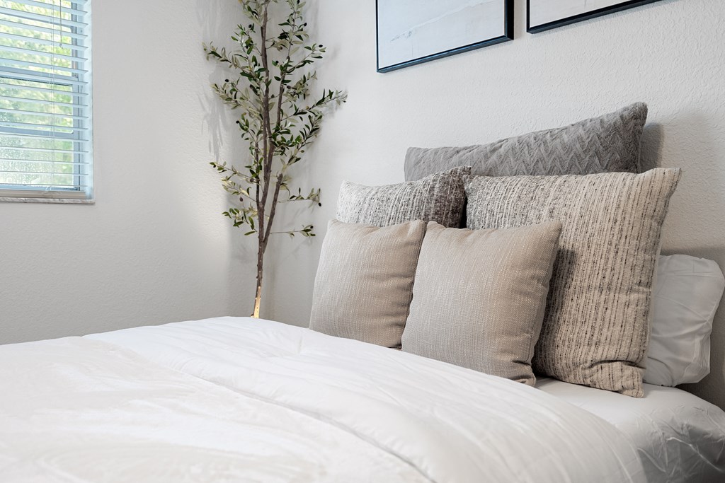 a bedroom with white bedding and pillows and a tree in the corner of the room