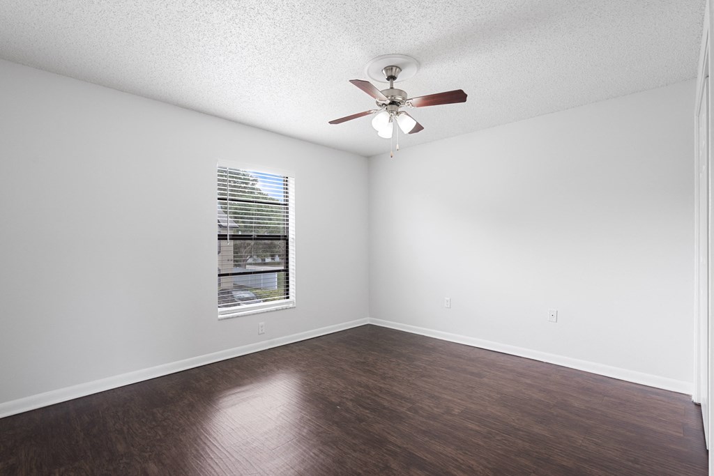 an empty bedroom with a ceiling fan and a window