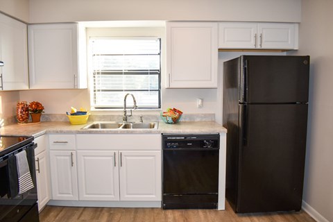A black refrigerator stands in a kitchen with white cabinets.