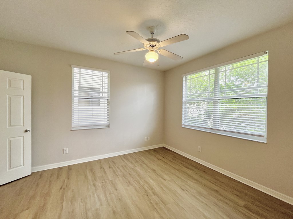 A room with a ceiling fan and two windows with blinds.