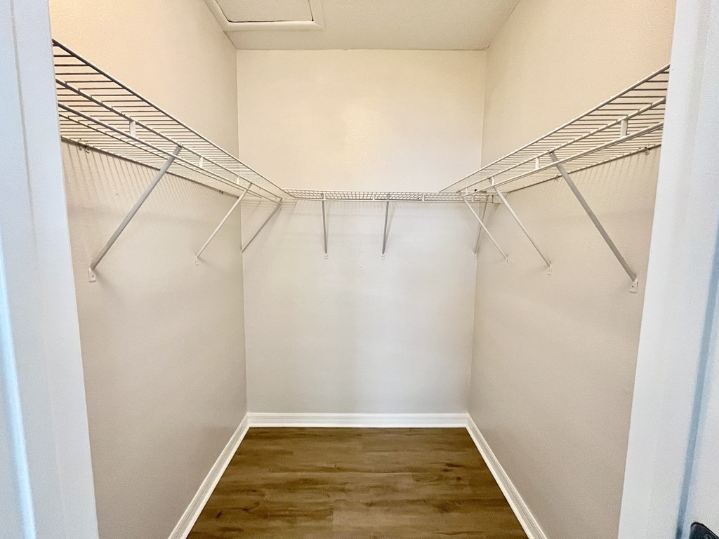 A walk-in closet with white walls and wooden floors.