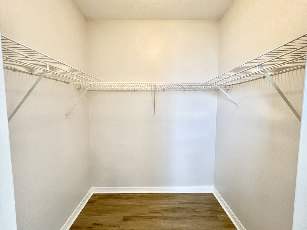 A white closet with a wooden floor and metal shelves.