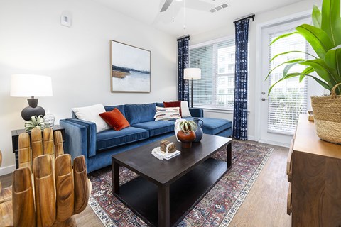 A living room with a blue couch, a wooden coffee table, and a painting on the wall.