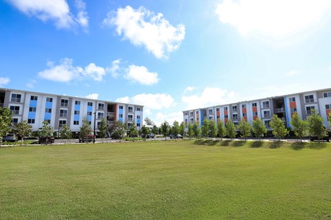 A grassy field in front of a row of apartment buildings.