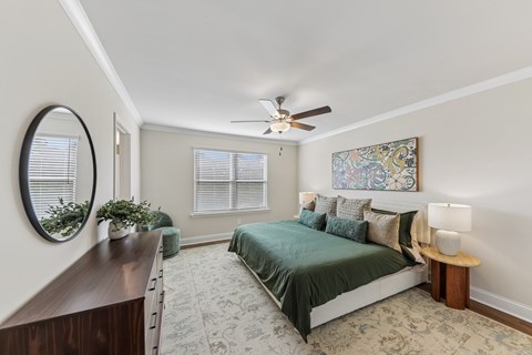 A bedroom with a bed, a mirror, a ceiling fan, and a window.