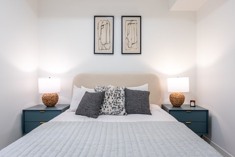 A bedroom with a large bed, two nightstands with lamps, and two framed artworks on the wall.