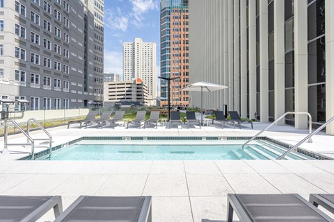 A pool surrounded by lounge chairs and umbrellas in a city setting.