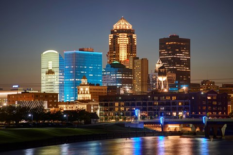 A city skyline at night with a bridge crossing a river in the foreground.