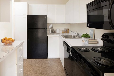A black refrigerator sits in a kitchen with white cabinets.