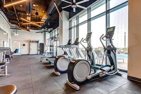 A gym with a row of stationary bikes and a fan overhead.