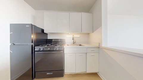 A kitchen with a black fridge, stove and white cabinets.