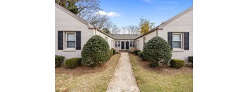 A house with a grey siding and black shutters is surrounded by green bushes.at Raleigh Rentals, Raleigh, NC, 27604