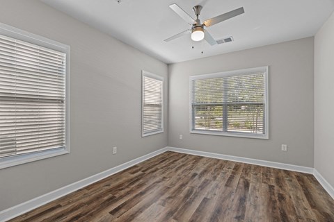 the spacious living room with a ceiling fan and two windows