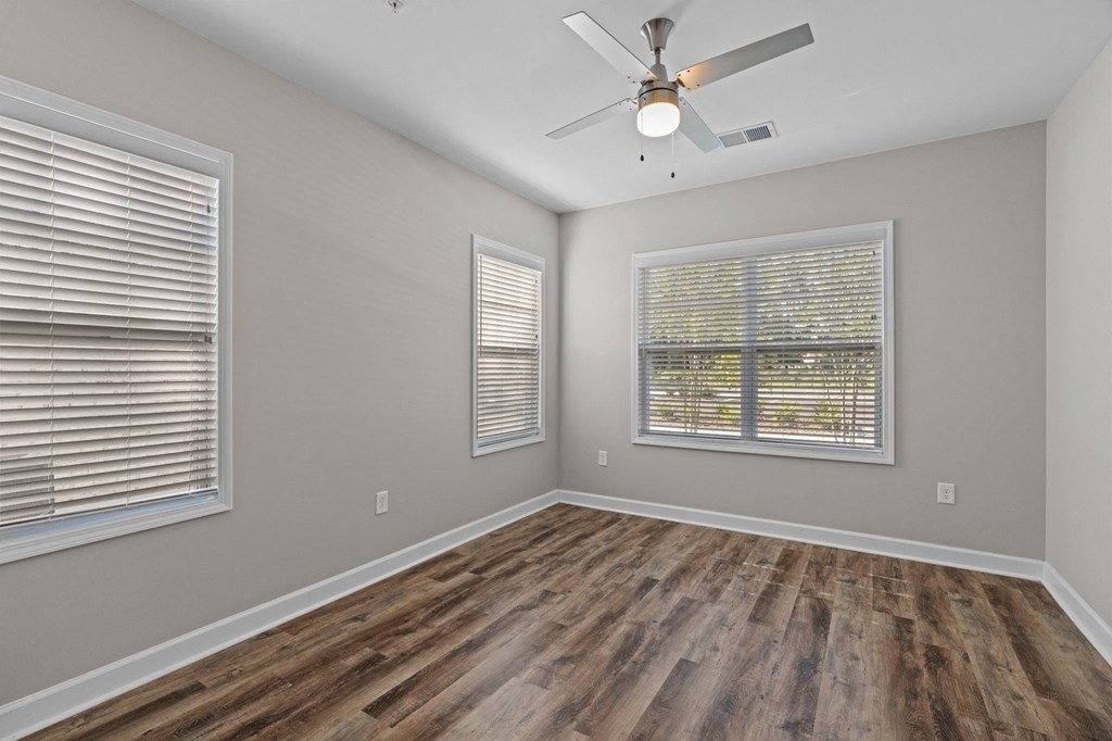 the spacious living room with a ceiling fan and two windows