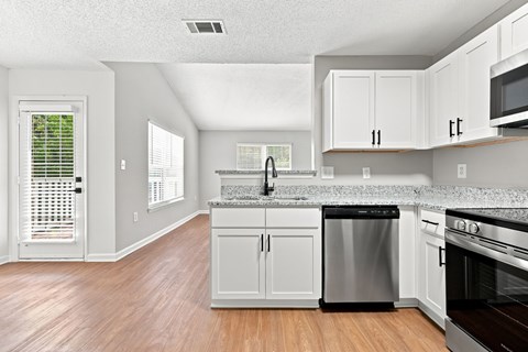 A kitchen with white cabinets and a wooden floor.