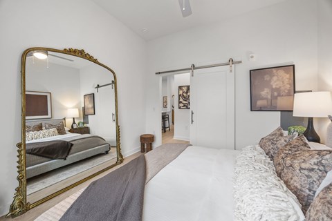 Bedroom with large gold mirror and barn door at Adler Montford Park + Drexel Townes Apartments, Charlotte, North Carolina