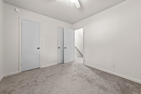 a bedroom with white walls and carpet and doors to a closet