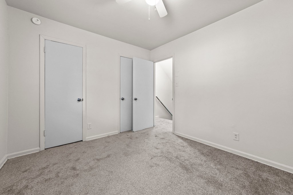 a bedroom with white walls and carpet and doors to a closet