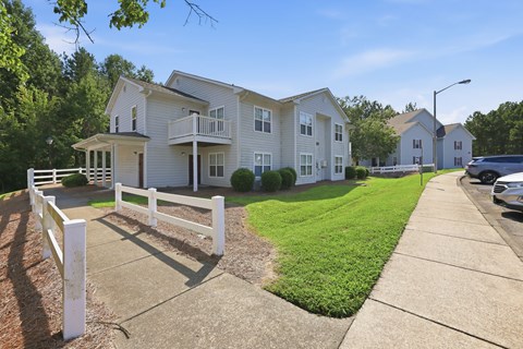 A white picket fence separates a driveway from a grassy area.