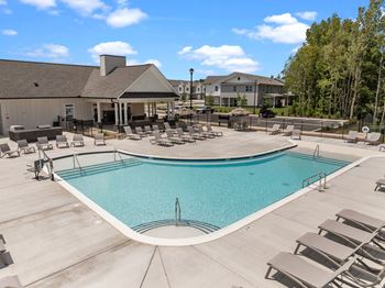 A large outdoor swimming pool surrounded by sun loungers and a building in the background at Regency Townes in Greenville, NC