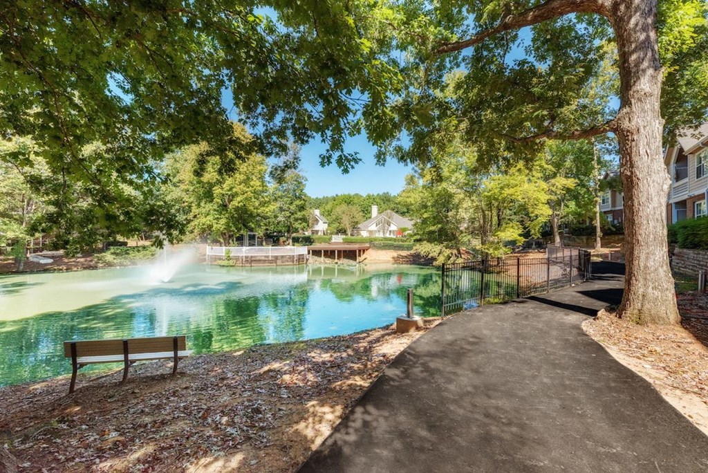 a fountain in a pond with trees and a bench
