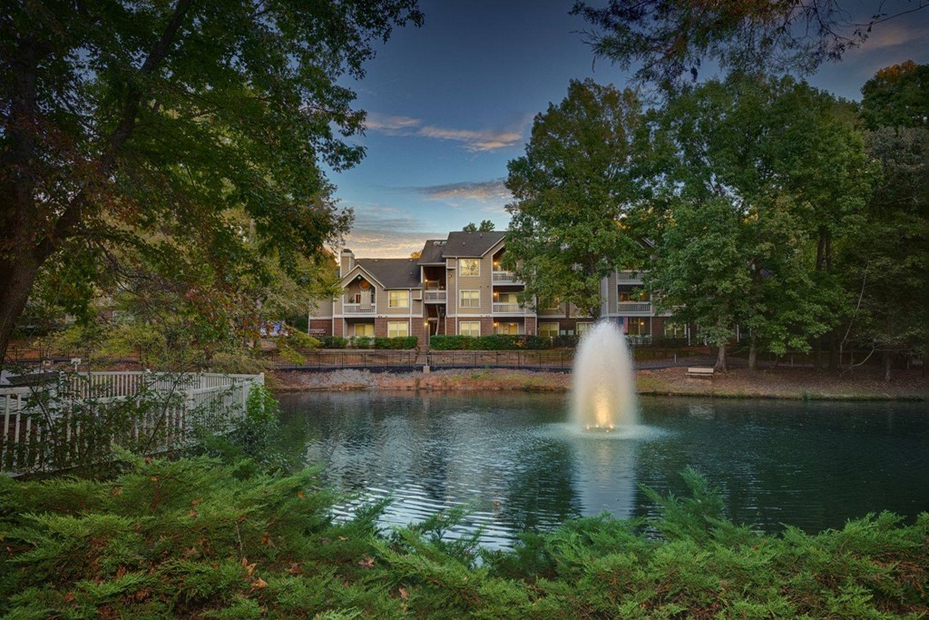 a fountain in a pond with an apartment building in the background