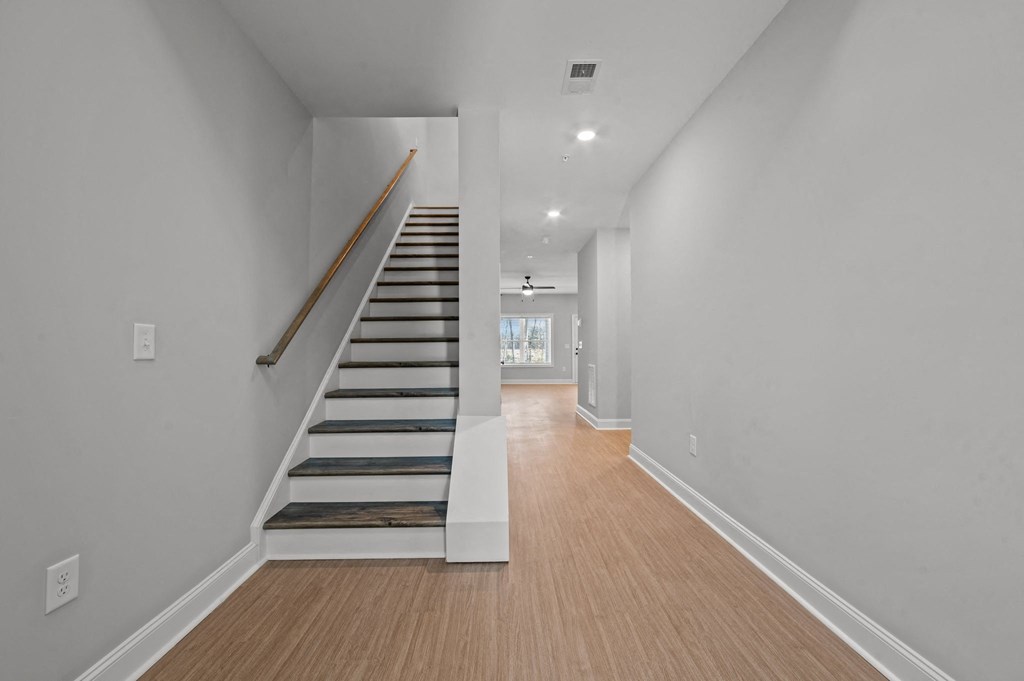 A long hallway with a staircase and wooden floors.at Regency Townes, Winterville, 28590