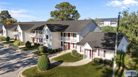 A white building with red doors and windows is surrounded by greenery.