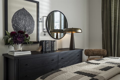 A bedroom with a dark blue bed and a round mirror above a dresser.