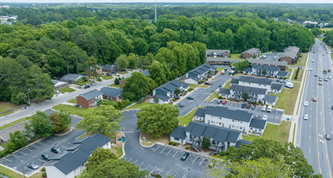 A road with cars and a parking lot with trees.