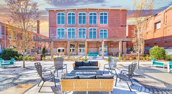 A courtyard with a wicker sofa and chairs in front of a red brick building at Judson Mill Lofts, South Carolina 29611